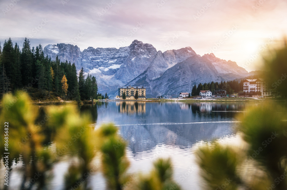 View of Misurina lake with large building of Institute Pius XII through bushes at sunset. Dolomites, Italy.