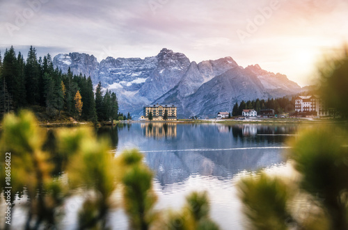 View of Misurina lake with large building of Institute Pius XII through bushes at sunset. Dolomites, Italy.