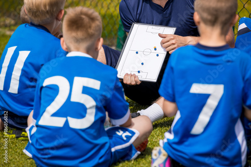 Coaching Kids Soccer. Football Team with Coach at the Stadium. Boys Listening to Coach's Instructions Before Competition. Coach Giving Team Talk Using Soccer Tactics Board