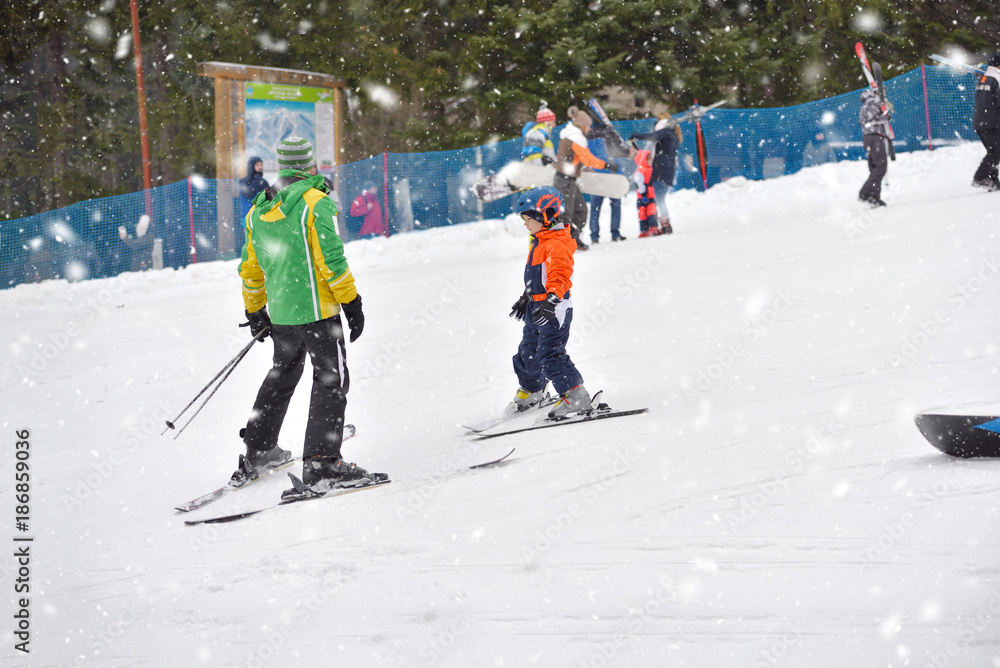Skiing boy learning from ski teacher, in ski suit and helmet on ski resort
