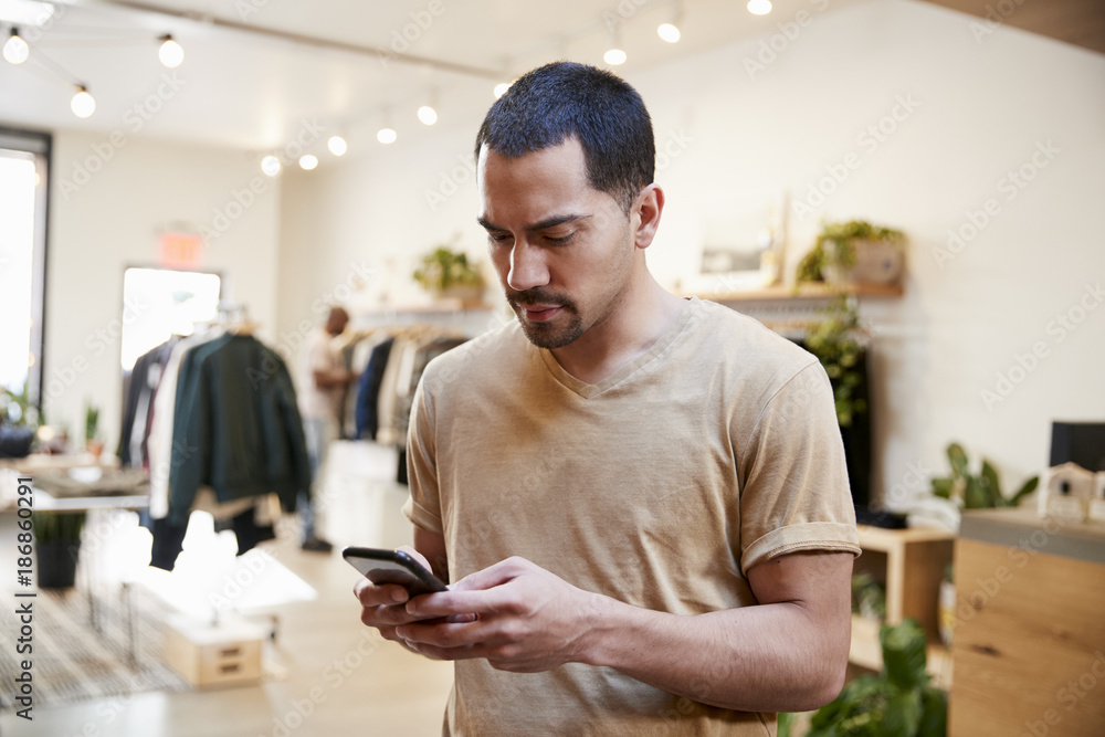 Young Hispanic man using smartphone in a clothes shop Young Hispanic man using smartphone in a clothes shop