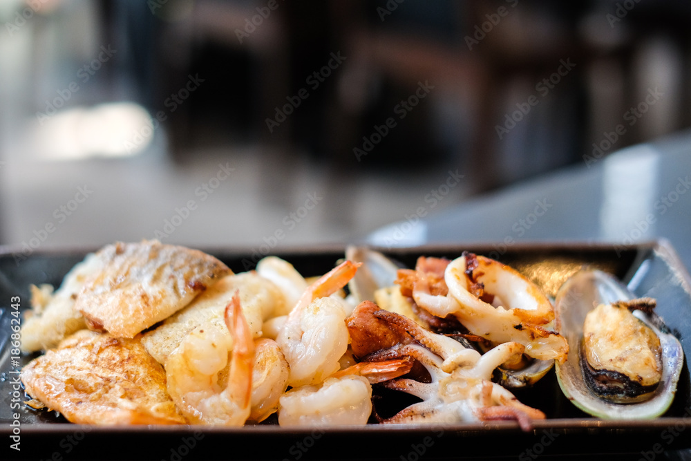 Grilled food (shrimp, squid or octopus, New Zealand mussel, salmon and dolly fish) serve on black plate for hot food background or texture - Party seafood concept.
