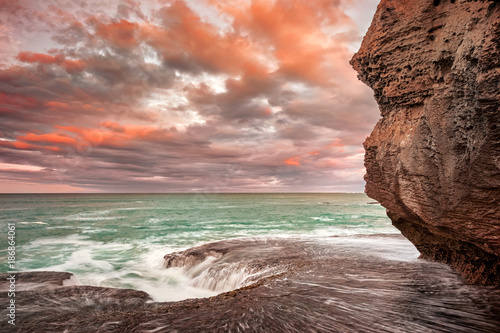 Orange clouds at sunrise over the sea from a sanstone rock shore photo