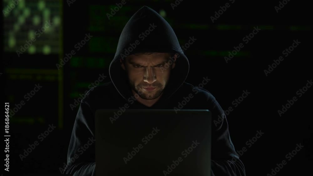 Stranger in dark sweatshirt with hood intently typing, gazing at monitor screen Stranger in dark sweatshirt with hood intently typing, gazing at monitor screen