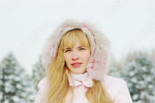 Portrait of a young beautiful woman wearing pink jacket with a hood in a winter park