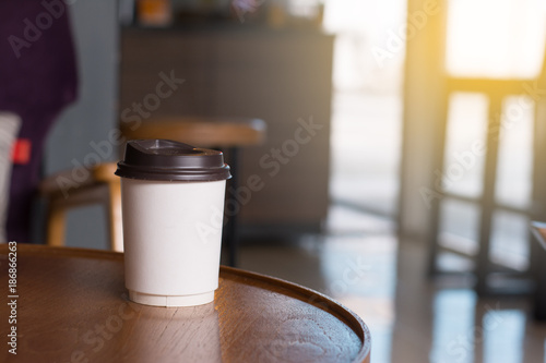 A white paper cup of hot beverage like cofee putting on wooden table in coffee shop with the light.