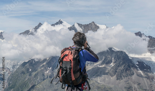 Rear view of male climber photographing low mountain clouds at Jegihorn, Valais, Switzerland photo