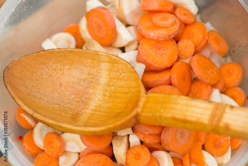 Natural wooden spoon in a bowl full of chopped vegetables - slices of carrot, pasternak and onions. Preparing soup for dinner. Healthy eating photo