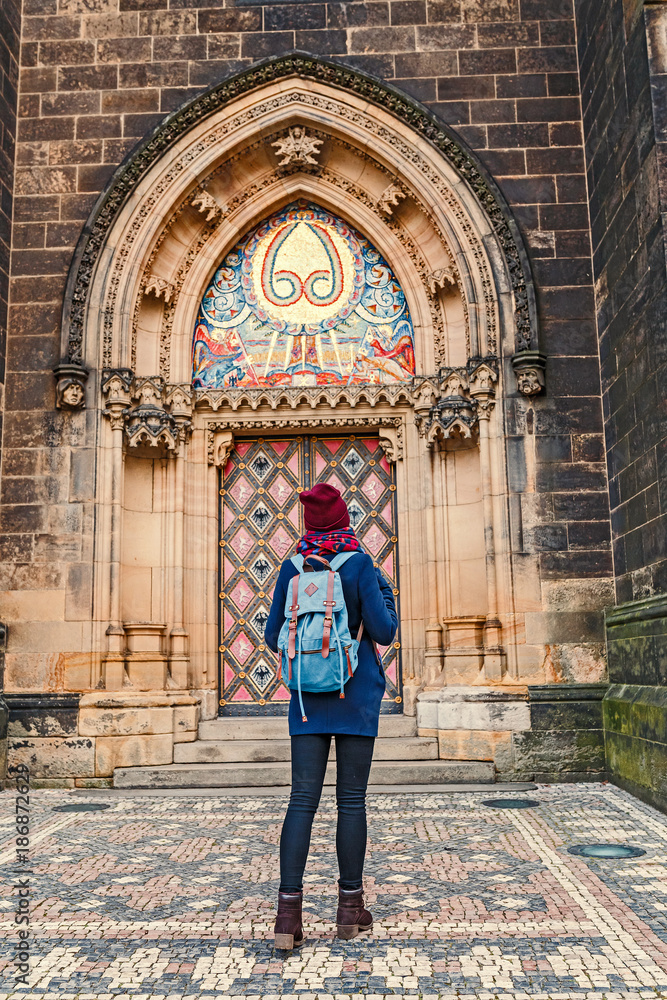 Pretty young female tourist with backpack looking at majestic Basilica of St. Peter and Paul in Prague