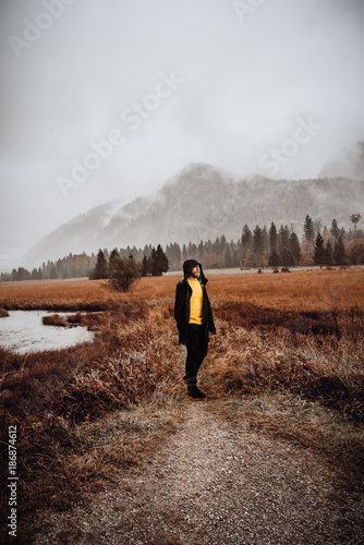 Mann in gelbem Pullover und schwarzer Jacke in regnerischer Berglandschaft photo