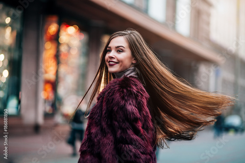 Young beautiful model girl smiles and looks back in the city. Dynamically young girl walks down the street.Hair fluttering in the wind.