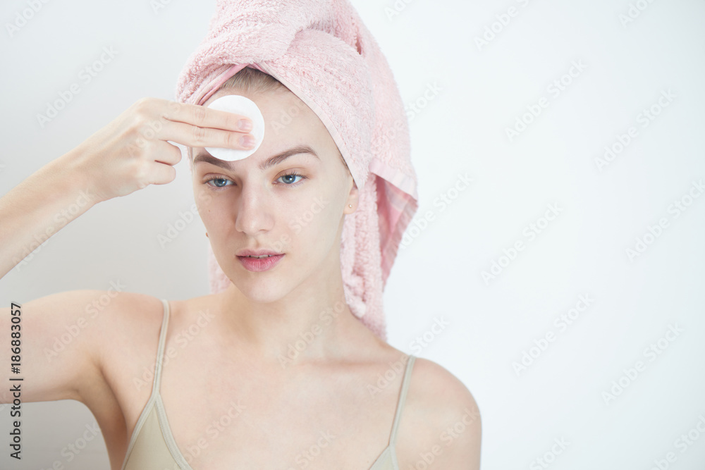 Facials. Girl with towel on head wipes clean the skin with a sponge on white background Facials. Girl with towel on head wipes clean the skin with a sponge on white background