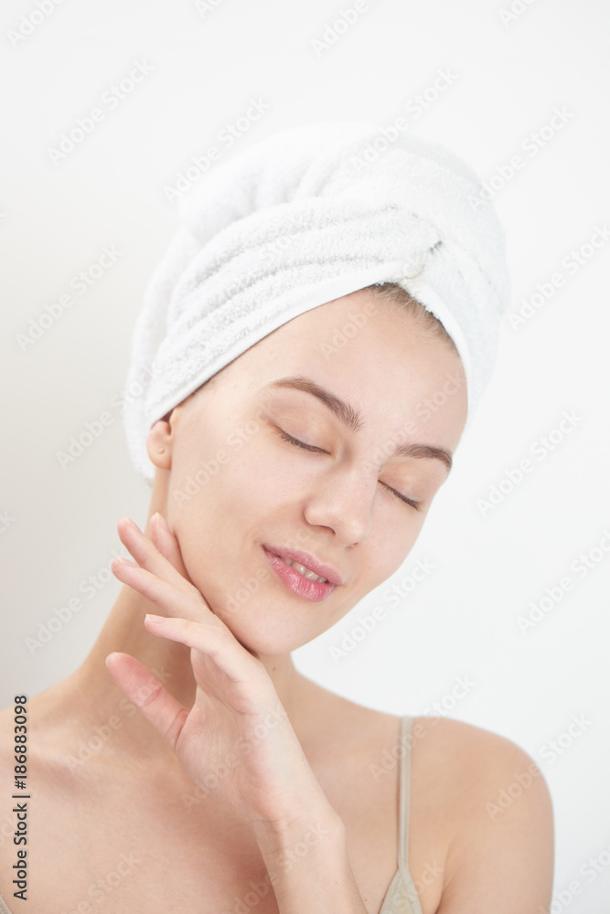 Skin care. Young woman on white background with towel on head touching her clean skin on the face