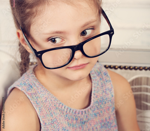 Happy smiling cute calm kid girl in eyeglasses in fashion colorful blouse looking. Closeup toned studio portrait