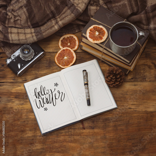 A beautiful composition on a winter theme with a mug of hot tea, a blanket, a diary and a pen. Added the text Hello winter.