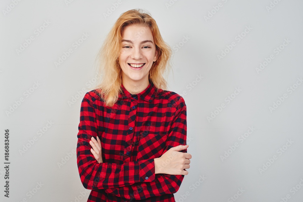 Portrait of young beautiful blonde. Girl in red shirt on white background. Student smiling with folded arms Portrait of young beautiful blonde. Girl in red shirt on white background. Student smiling with folded arms