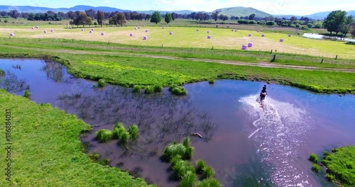 Aerial, horseback rider speeds through pond in Australia