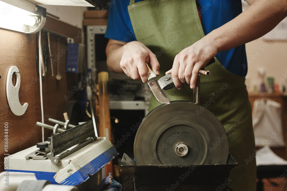 Making of a knife. Master sharpens a blade on the machine closeup in the Studio Making of a knife. Master sharpens a blade on the machine closeup in the Studio