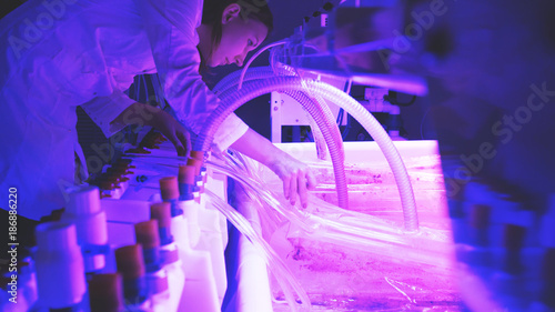 A woman scientist in a lab coat conducting an experiment in a lab with purple lightning and a large tank of liquid. © diproduction