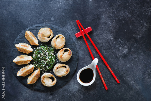 Stone slate with pan fried asian dumplings served with chuka salad. Flat-lay on a dark scratched metal background with space, horizontal shot