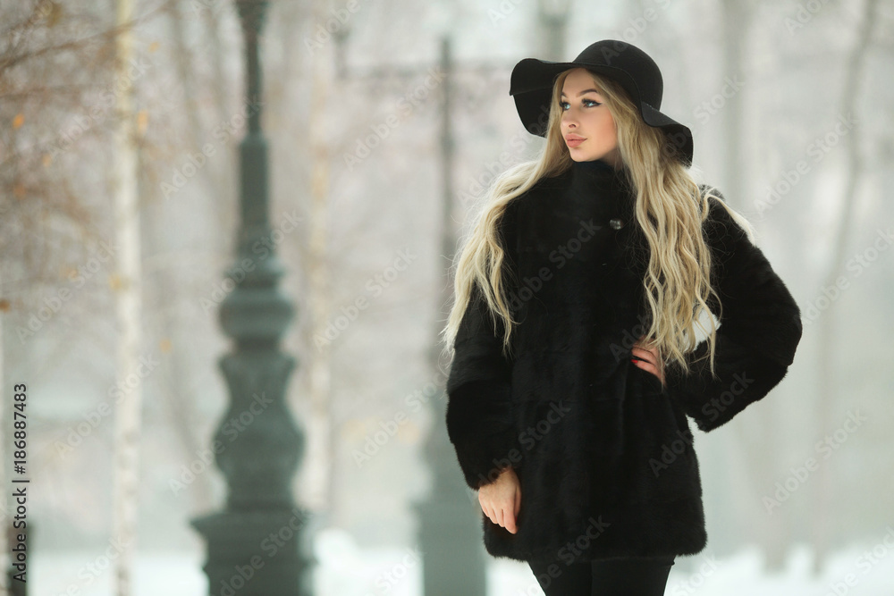 beautiful young girl in fur coat and hat walking in snow park beautiful young girl in fur coat and hat walking in snow park