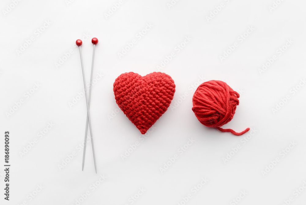 a knitted heart of red thread with an inserted knitting needle on a white background. and a hank of a red knitting thread a knitted heart of red thread with an inserted knitting needle on a white background. and a hank of a red knitting thread