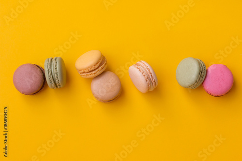 Set of tasty macarons with pieces of nuts on yellow background.