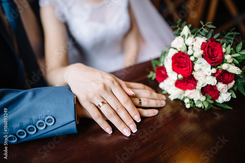 bride and groom in a cafe. wedding bouquet of roses on a wooden table in a restaurant, bride and groom hold each other's hands. Wedding rings. Loving couple in a cafe. hot tea for lovers. closeup view photo