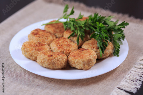 Fried cutlets on a white plate on a table on a gray background.