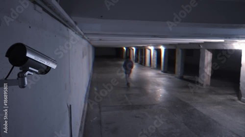 Kind of dangerous person walking at night on an underground passage in the background of a surveillance camera