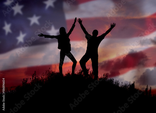 Two people against the American flag Full length silhouette of a happy couple stand together on top of a mountain with their hands up, Man and woman on top of a mountain of freedom.Democracy