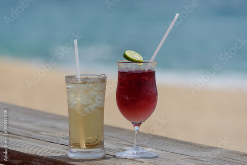 Two iced alcoholic beverages, in frosty glasses, with beach and surf in background.