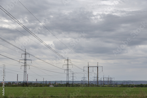 high-voltage power transmission lines in a green flat field against a cloudy sky.
