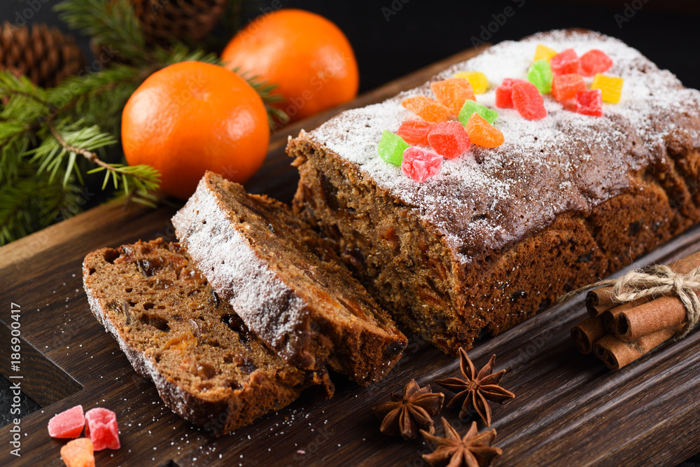 Freshly backed fruit cake with raisins, prunes and dried apricots decorated with candied fruits on dark oak board
