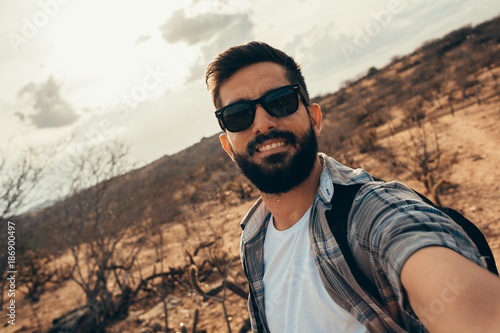 Man traveling with backpack hiking in desert. Travel lifestyle success concept. Man doing self portrait