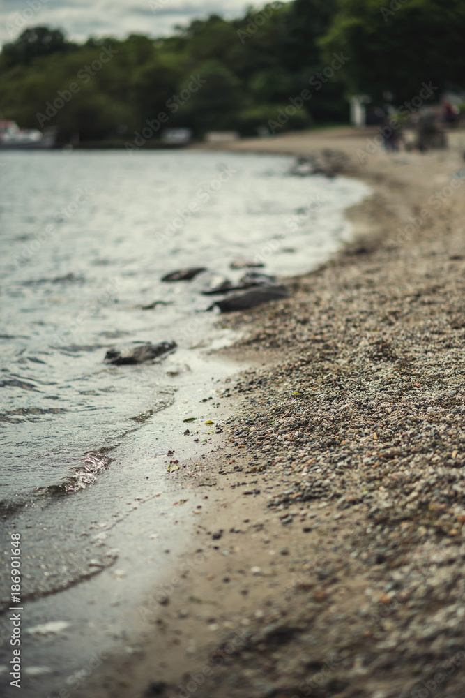 A close shot of water on a lake shore, with details of bubbles and little stones on the sand A close shot of water on a lake shore, with details of bubbles and little stones on the sand