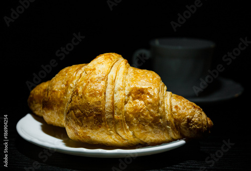 croissants on plate and cup of tea or coffee on dark wooden background
