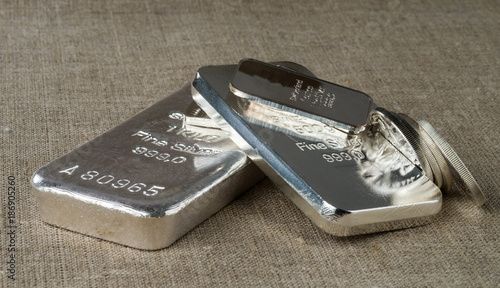 Silver bullion (bars and coins) on a background of a rough wooden texture. .