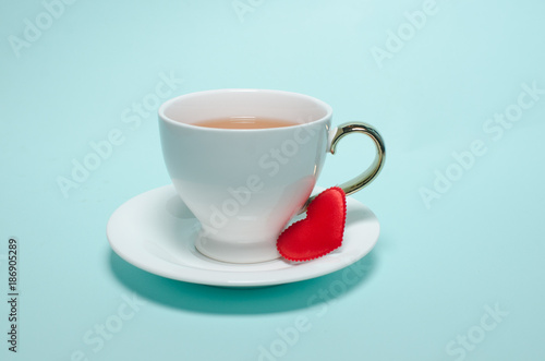 Two white cups and a red heart on Valentine's Day stand on a turquoise background. Valentine's day card