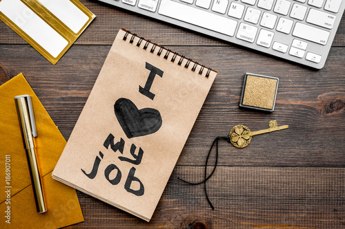 Positive attitude to work. I love my job written in notebook near stationery at office desk on dark wooden background top view photo