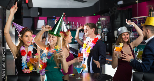Portrait of cheerful women and men in caps with cocktails