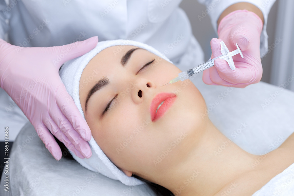 The doctor cosmetologist makes the Rejuvenating facial injections procedure for tightening and smoothing wrinkles on the face skin of a beautiful, young woman in a beauty salon.Cosmetology skin care. The doctor cosmetologist makes the Rejuvenating facial injections procedure for tightening and smoothing wrinkles on the face skin of a beautiful, young woman in a beauty salon.Cosmetology skin care.