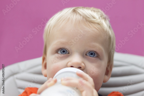 Close up portrait of blue-eyed toddler drinking his bottle