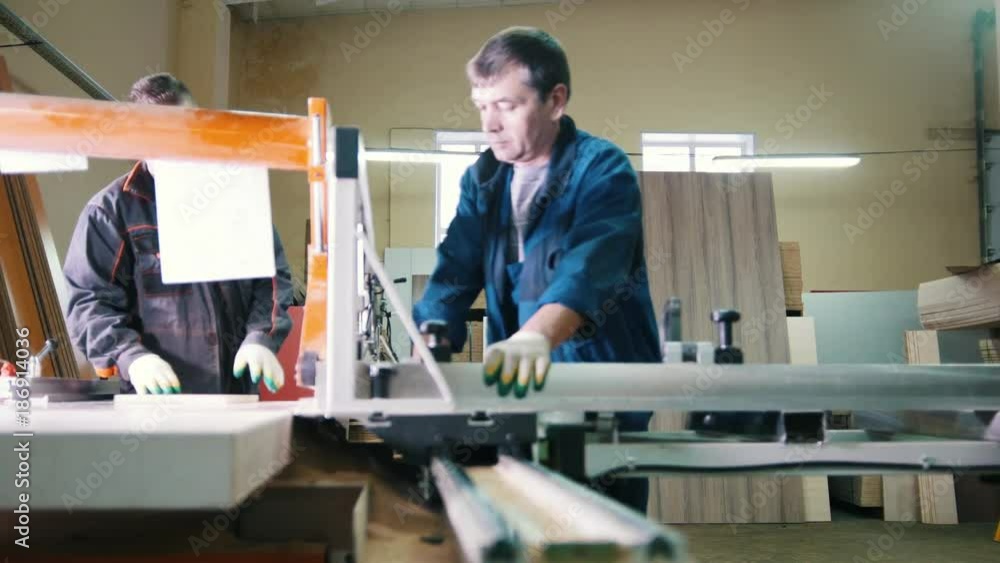 Workers carpenters are cutting wood board on electric saw at furniture factory Workers carpenters are cutting wood board on electric saw at furniture factory