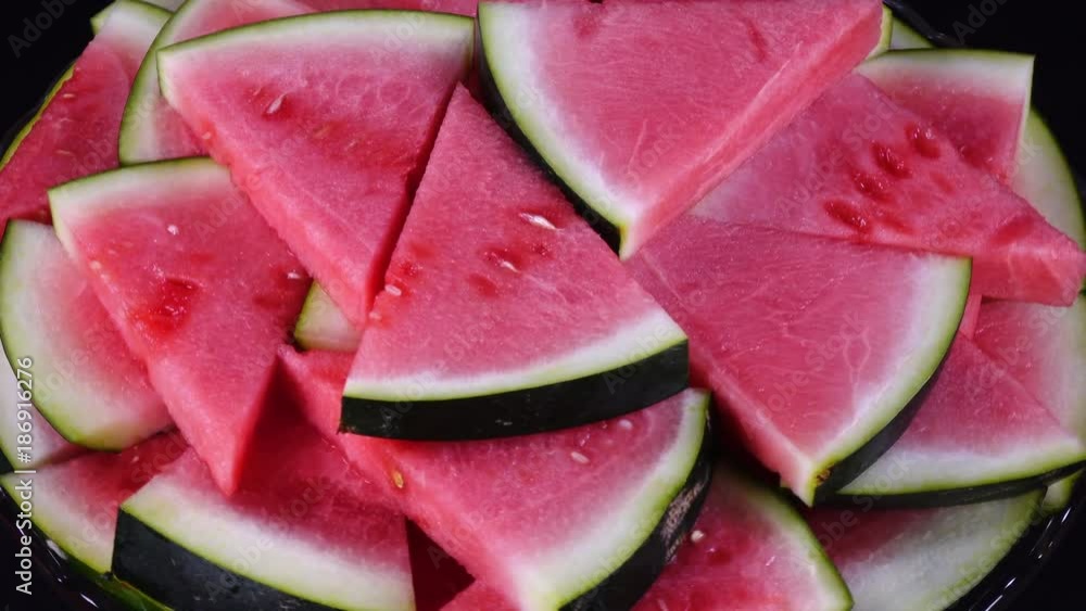 Excellent heap of fresh red water melon in triangle pieces on glass plate, rotating against the clock. Vibrant batch of yummy fruit pieces on black background with amazing texture in UHD 4k clip. Excellent heap of fresh red water melon in triangle pieces on glass plate, rotating against the clock. Vibrant batch of yummy fruit pieces on black background with amazing texture in UHD 4k clip.