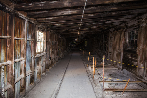 A long narrow hallway of bare wood beams and rafters with a sloped roof and a cement floor of an abandoned factory