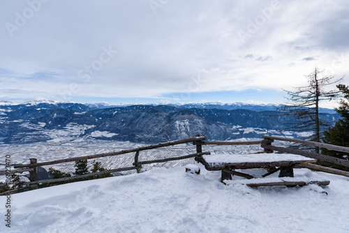Wallpaper Mural Snowy Adige valley seen from above. View of landscape of the alpine city between mountains, South Tyrol, Trentino. Aerial view of a valley.Valley full of snow. A bench and a table in the foregound Torontodigital.ca