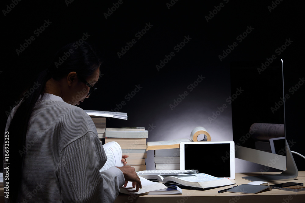 Girl in white shirt reading many textbooks on table with many high stacking