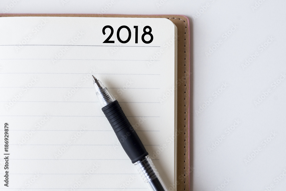 Conceptual,notebook on a white table. open diary and pen with 2018 words Conceptual,notebook on a white table. open diary and pen with 2018 words