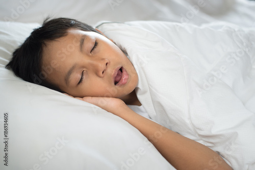 young boy sleeping with mouth open (snoring) on bed white pillow and sheet.boy asleep and snoring.sleep concept
